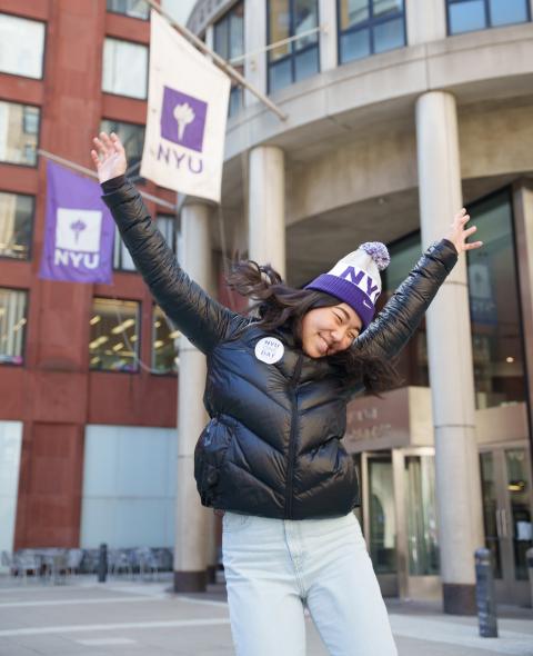 A student celebrates NYU One Day in front of NYU Stern