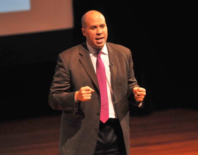 Senator Cory Booker speaking at Business & Its Publics Plenary Man in a suit speaking on a stage