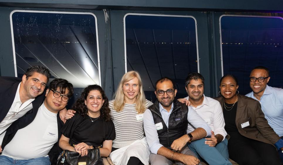 A group of 8 people sitting next to each other with the windows of the boat behind them