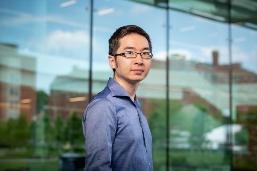 Photo of Professor Qiaochu Wang in front of a glass building