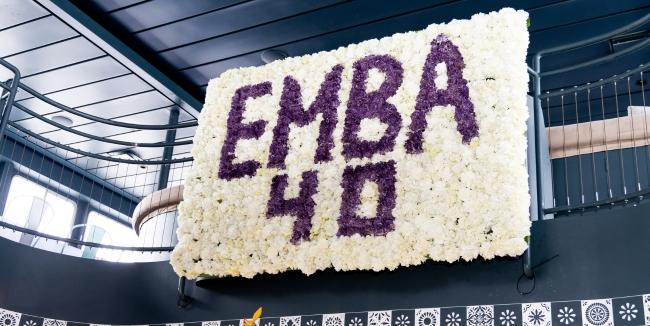 A white flower wall that reads "EMBA 40" in purple flowers