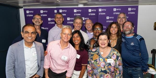 A group of 12 smiling people standing in front of a step-and-repeat that says "NYU Stern"