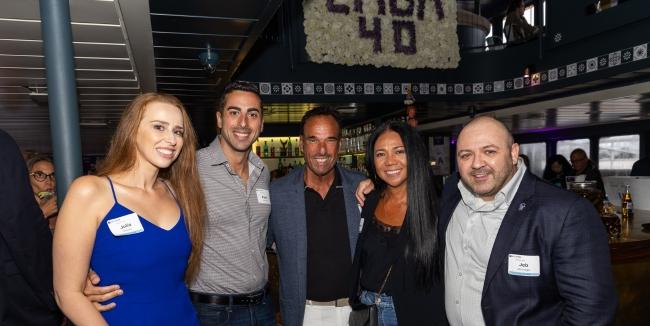 A group of five smiling people stand together with a flower wall behind them that says "EMBA 40"