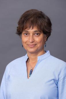 A headshot photo of a smiling Shama Patel taken against a studio backdrop